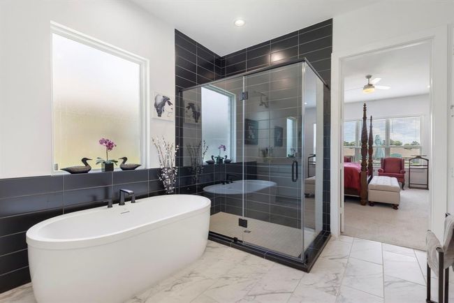 This modern bathroom features a sleek freestanding bathtub, a spacious glass-enclosed shower with dark tile accents, and marble flooring. It opens into a bright bedroom, creating a seamless and elegant connection between spaces. | Image 29