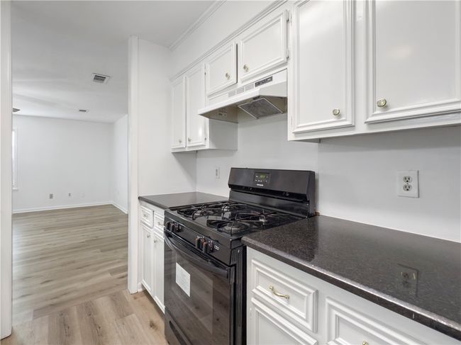 Kitchen with black gas range oven, under cabinet range hood, dark countertops, light wood-type flooring, and white cabinets | Image 8
