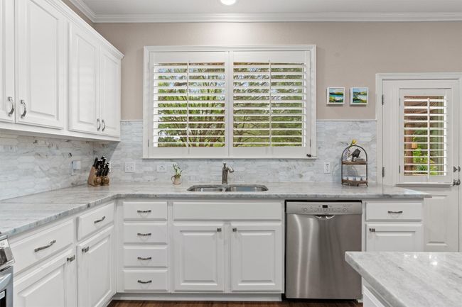 Kitchen with dishwasher, a sink, ornamental molding, white cabinetry, and decorative backsplash | Image 11