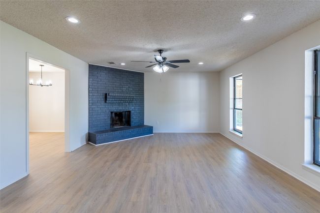 Unfurnished living room featuring a textured ceiling, recessed lighting, ceiling fan with notable chandelier, wood finished floors, and a fireplace | Image 24