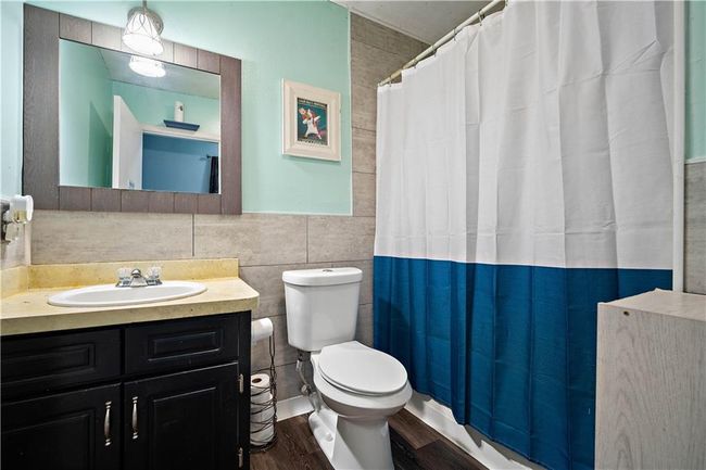 Full bathroom featuring vanity, toilet, tile walls, curtained shower, and wood finished floors | Image 16