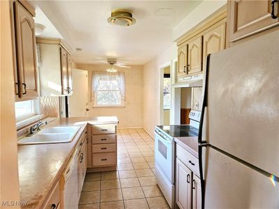 Kitchen with light brown cabinets, ceiling fan, light tile patterned flooring, sink, and white appliances | Image 2