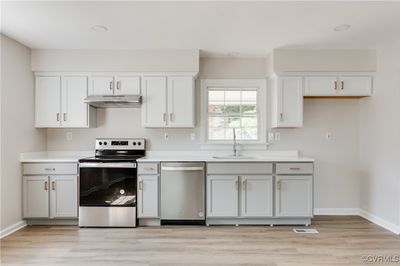 Kitchen with light wood-type flooring, appliances with stainless steel finishes, sink, and white cabinetry | Image 1