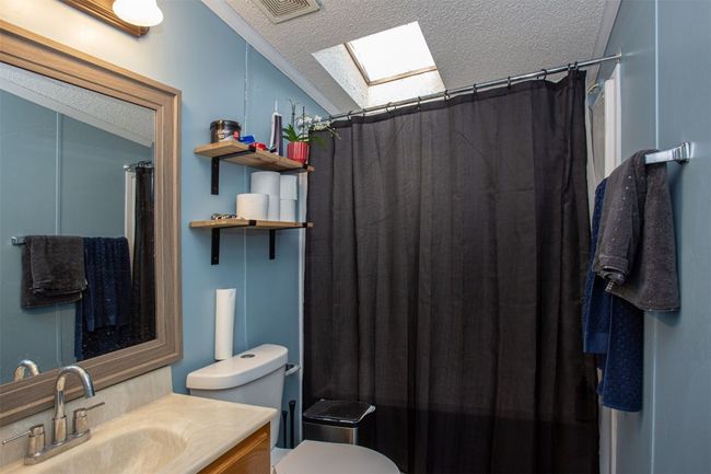 Bathroom with a skylight, vanity, a textured ceiling, toilet, and curtained shower | Image 12
