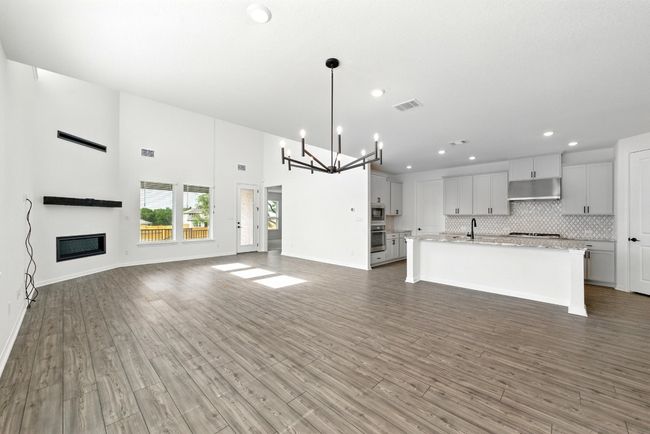 Unfurnished living room with a chandelier, recessed lighting, a glass covered fireplace, wood finished floors, and baseboards | Image 9