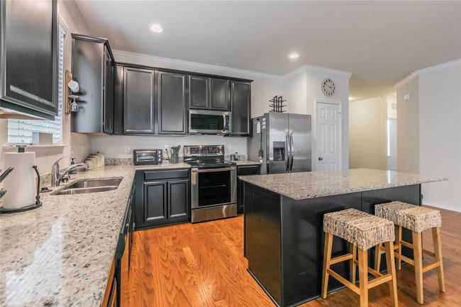 Kitchen featuring a breakfast bar, sink, light stone counters, a kitchen island, and stainless steel appliances | Image 16