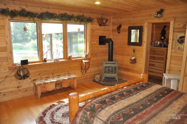 Bedroom featuring a wood stove, multiple windows, wood walls, wood finished floors, and wood ceiling | Image 10