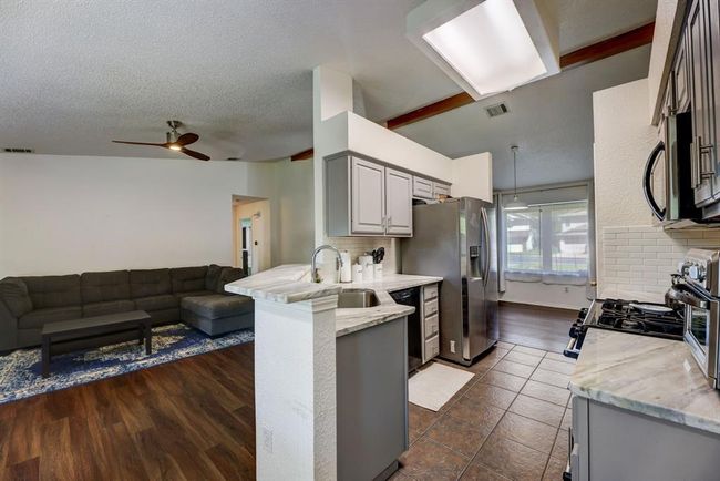 Kitchen with open floor plan, a peninsula, a sink, a ceiling fan, and light stone counters | Image 5