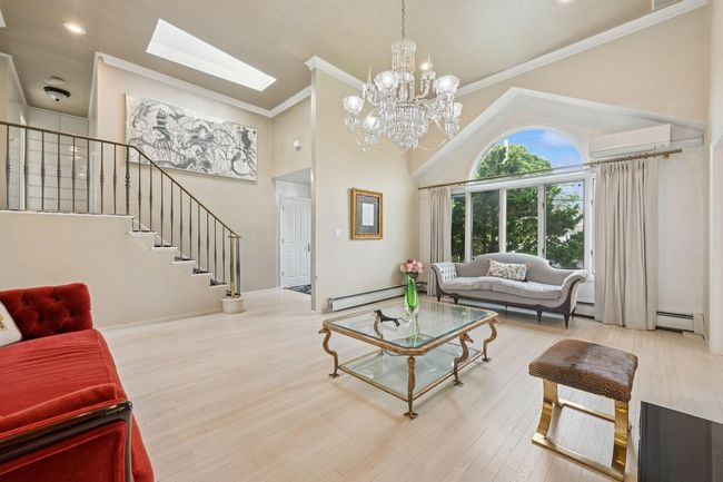 Living room with a baseboard heating unit, stairs, a wall mounted air conditioner, a chandelier, and wood finished floors | Image 6