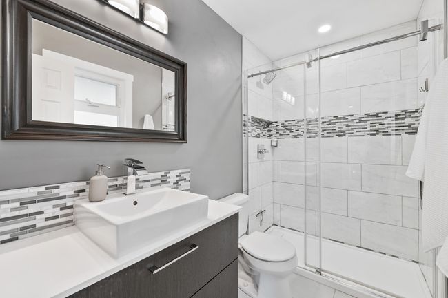 Full bath featuring a shower stall, vanity, toilet, and decorative backsplash | Image 27