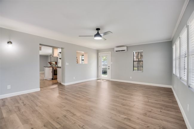 Unfurnished living room with a wall mounted AC, ceiling fan, ornamental molding, and light wood-style floors | Image 9