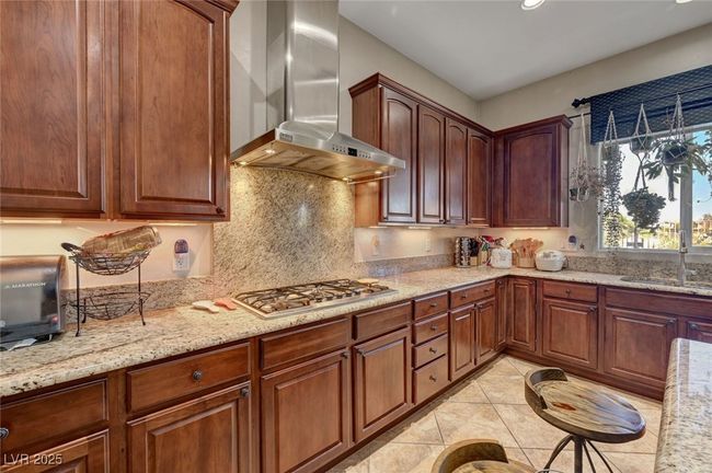 Kitchen featuring wall chimney range hood, stainless steel gas cooktop, light stone counters, light tile patterned floors, and decorative backsplash | Image 17