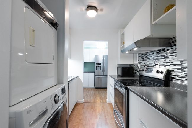Kitchen featuring white cabinets, stacked washer / dryer, light wood-type flooring, and appliances with stainless steel finishes | Image 13
