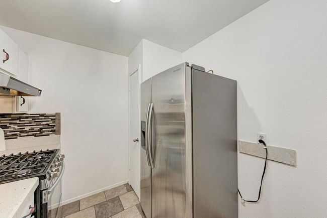 Kitchen featuring under cabinet range hood, tasteful backsplash, stone tile flooring, appliances with stainless steel finishes, and light countertops | Image 16