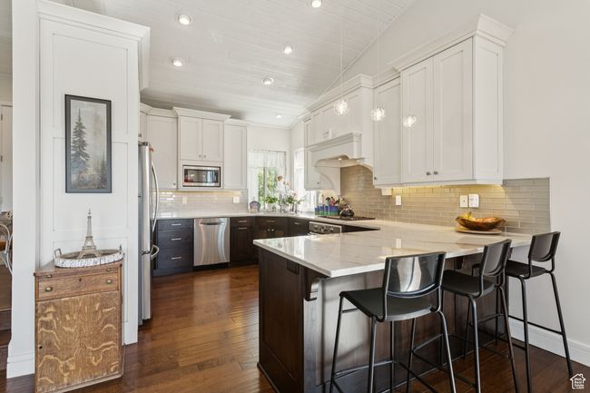 Kitchen with appliances with stainless steel finishes, a peninsula, white cabinets, dark wood finished floors, and decorative backsplash | Image 7