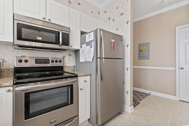 Kitchen with appliances with stainless steel finishes, crown molding, white cabinets, backsplash, and wallpapered walls | Image 6