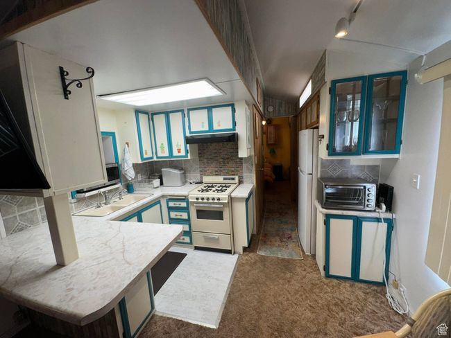 Kitchen featuring white appliances, under cabinet range hood, light countertops, backsplash, and carpet flooring | Image 12