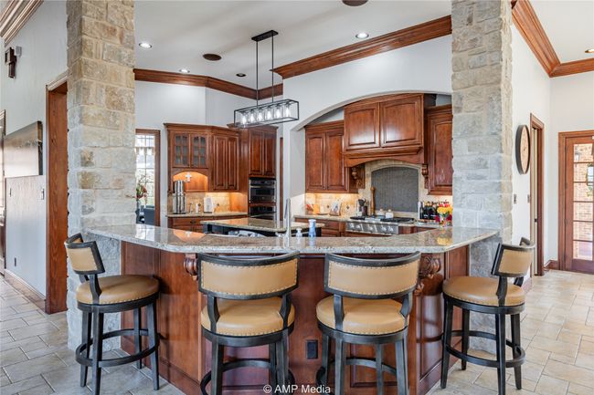 Kitchen with light stone countertops, kitchen peninsula, appliances with stainless steel finishes, and ornate columns | Image 14