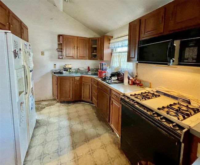 Kitchen with vaulted ceiling, white fridge with ice dispenser, black microwave, gas range, and light floors | Image 5