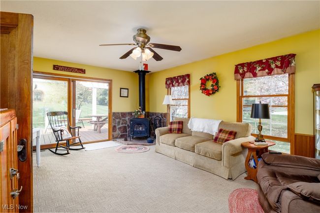Carpeted living area with wainscoting, a wood stove, and ceiling fan | Image 13