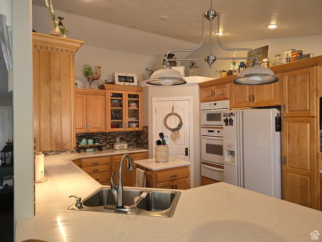 Kitchen with glass insert cabinets, a sink, light countertops, white appliances, and backsplash | Image 20