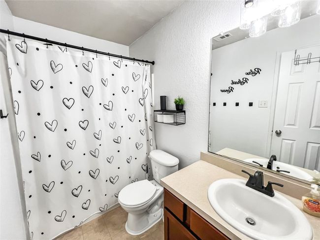 Bathroom with toilet, a textured wall, vanity, a shower with shower curtain, and tile patterned floors | Image 7