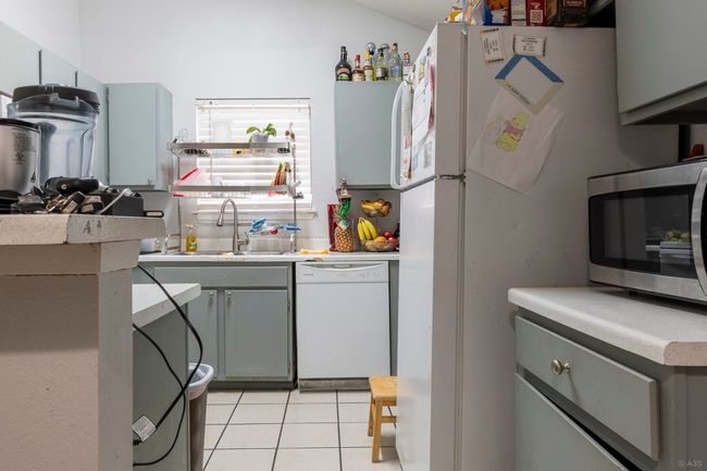 Kitchen with white dishwasher, stainless steel microwave, a sink, gray cabinets, and light tile patterned floors | Image 5
