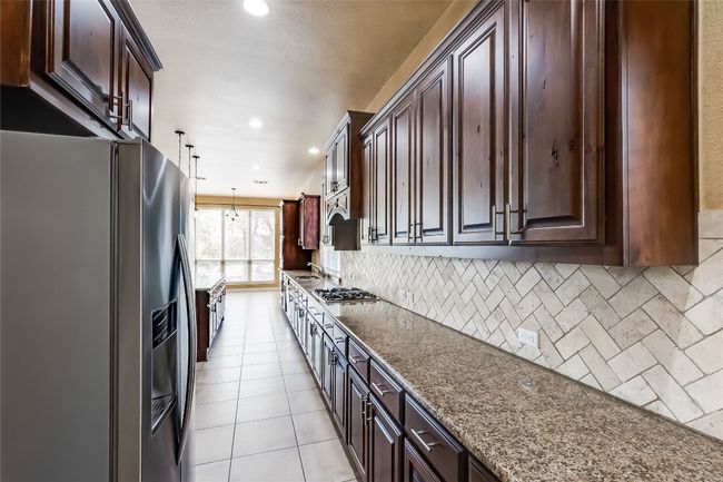 Kitchen featuring light tile patterned flooring, a sink, tasteful backsplash, appliances with stainless steel finishes, and dark brown cabinets | Image 16