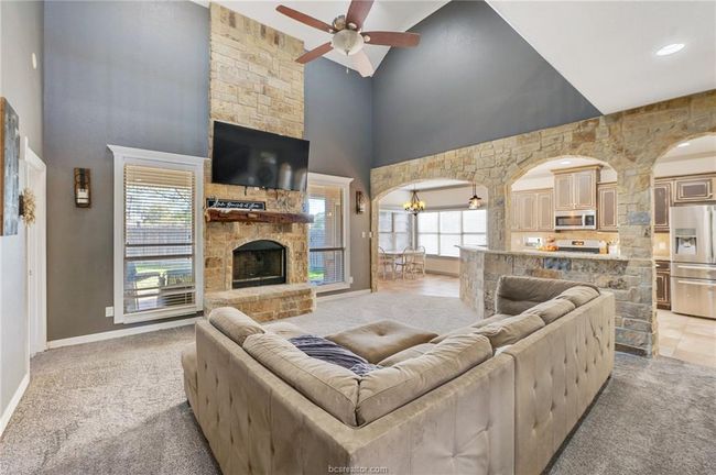 Living area with high vaulted ceiling, light colored carpet, a ceiling fan, a stone fireplace, and arched walkways | Image 7