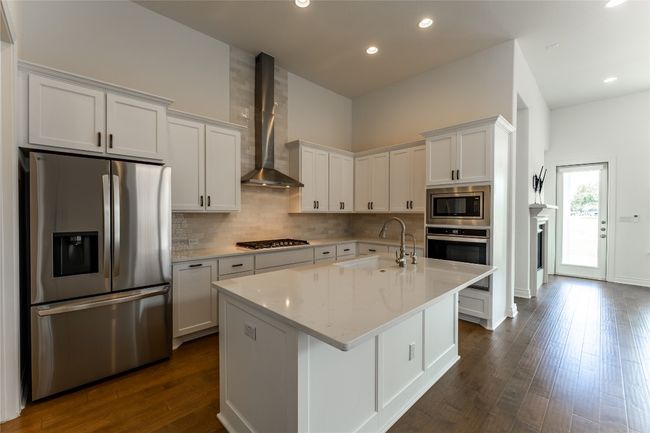 Kitchen featuring stainless steel appliances, wall chimney range hood, decorative backsplash, dark wood finished floors, and white cabinetry | Image 12