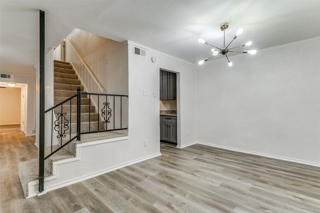 Empty room featuring crown molding, stairs, wood finished floors, a notable chandelier, and visible vents | Image 4