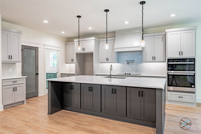 Kitchen featuring sink, premium range hood, an island with sink, black electric cooktop, and stainless steel double oven | Image 7