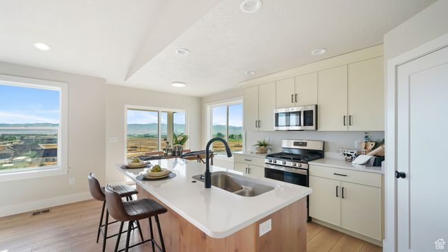 Kitchen featuring stainless steel appliances, recessed lighting, light wood-style flooring, light countertops, and a center island with sink | Image 10
