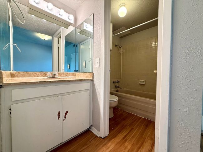 Bathroom with wood finished floors, vanity, washtub / shower combination, a textured ceiling, and a textured wall | Image 11
