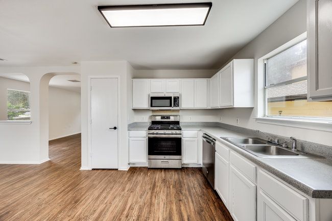 Kitchen featuring appliances with stainless steel finishes, a sink, white cabinets, and wood finished floors | Image 16