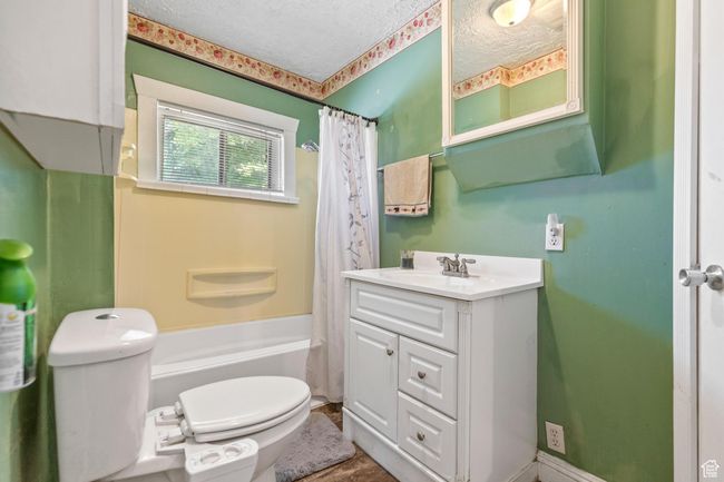 Full bath featuring toilet, a textured ceiling, vanity, and shower / bath combo | Image 16