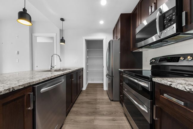 Kitchen featuring stainless steel appliances, a sink, dark brown cabinets, light stone countertops, and recessed lighting | Image 27