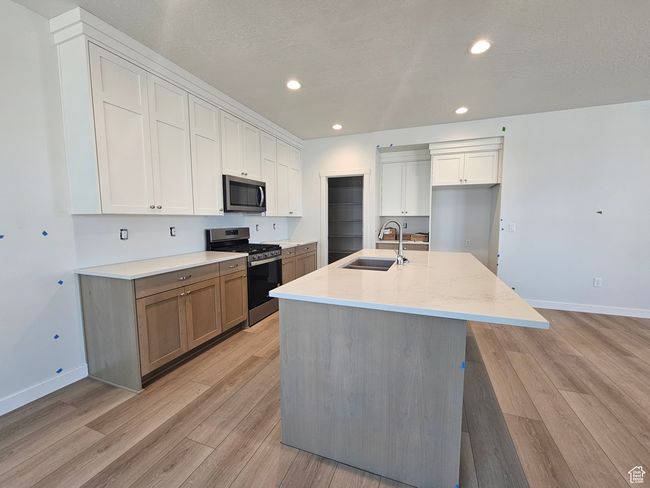 Kitchen with appliances with stainless steel finishes, light wood-style floors, white cabinets, an island with sink, and recessed lighting | Image 8