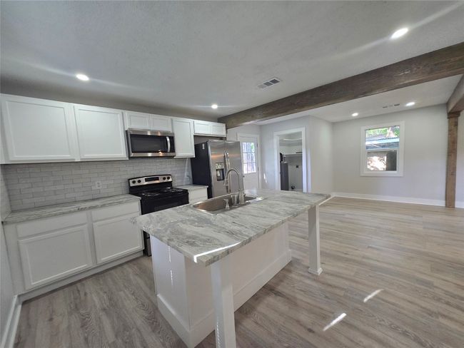 Kitchen featuring appliances with stainless steel finishes, white cabinetry, tasteful backsplash, light wood-style floors, and plenty of natural light | Image 9