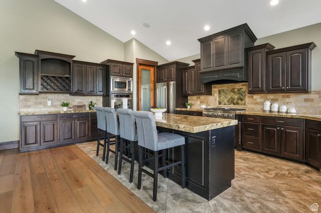 Kitchen with lofted ceiling, a kitchen island, dark brown cabinetry, a kitchen bar, and appliances with stainless steel finishes | Image 10