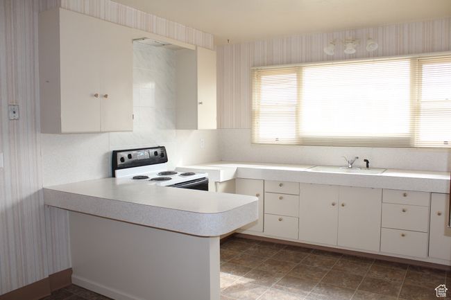 Kitchen featuring white range with electric cooktop, light countertops, a peninsula, white cabinetry, and wallpapered walls | Image 4