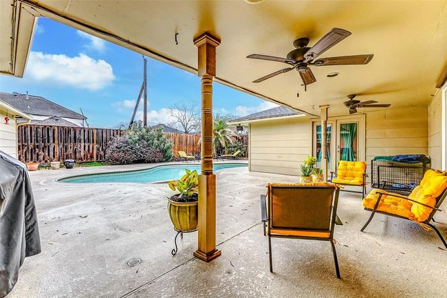 This spacious covered patio offers plenty of room for a large seating arrangement or an outdoor dining setup. Twin ceiling fans provide a refreshing breeze, making it an ideal spot to relax or gather while enjoying the nearby pool. | Image 35