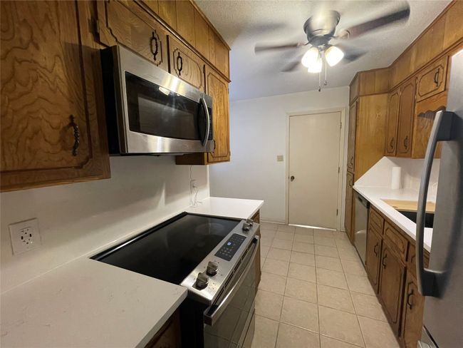 Kitchen featuring appliances with stainless steel finishes, light countertops, brown cabinets, and light tile patterned floors | Image 15