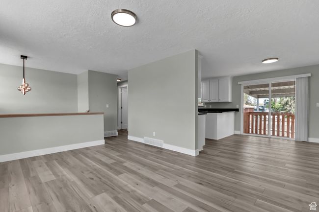 Unfurnished living room featuring a chandelier, light wood finished floors, baseboards, visible vents, and a textured ceiling | Image 10