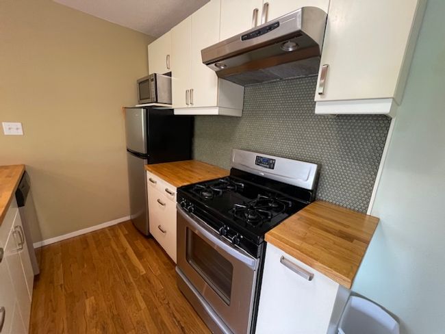 Kitchen featuring appliances with stainless steel finishes, under cabinet range hood, butcher block counters, and white cabinetry | Image 4