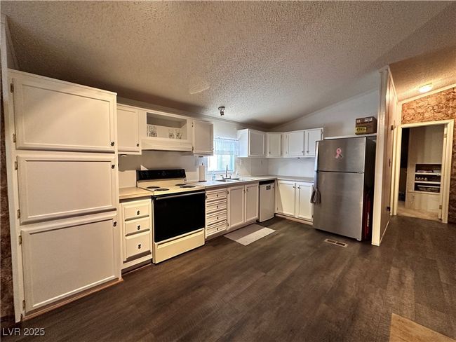 Kitchen featuring freestanding refrigerator, range with electric stovetop, a sink, a textured ceiling, and dishwashing machine | Image 6