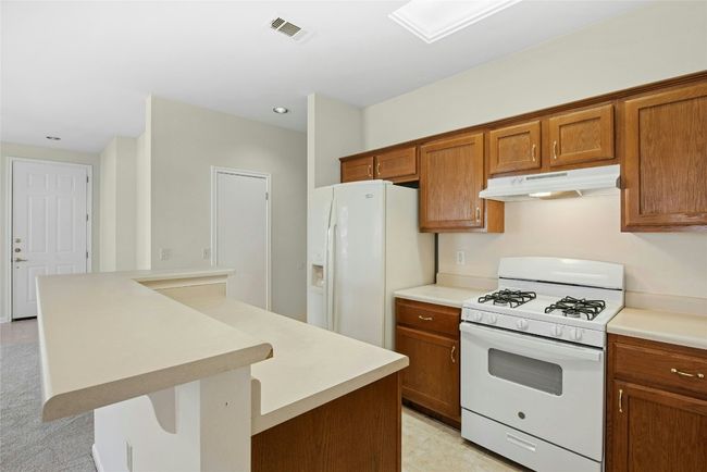 Kitchen with white appliances, under cabinet range hood, brown cabinets, a peninsula, and a kitchen breakfast bar | Image 12