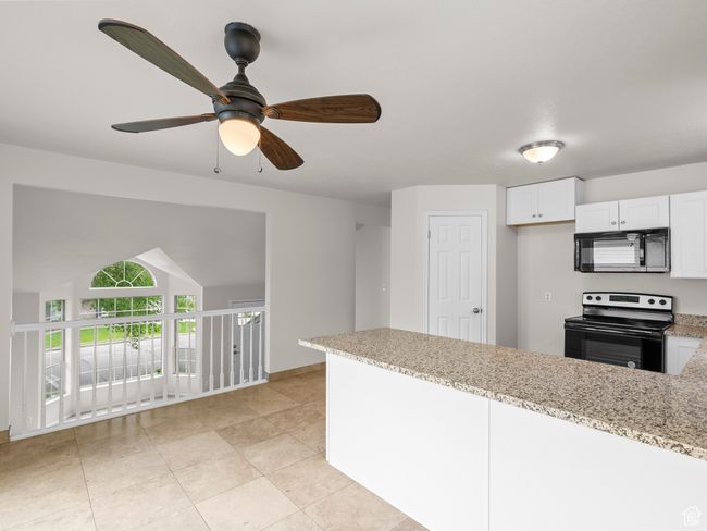 Kitchen featuring range with electric stovetop, black microwave, a peninsula, light stone countertops, and ceiling fan | Image 12