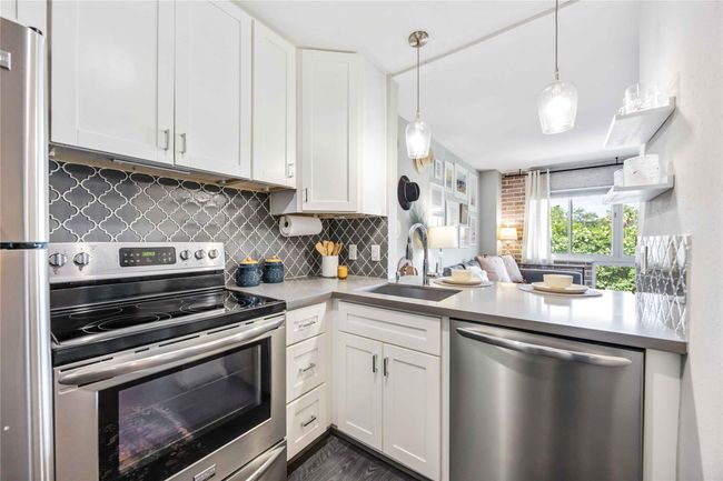 This fully remodeled kitchen features sleek stainless steel appliances, white cabinetry, and a stylish dark geometric backsplash. | Image 4