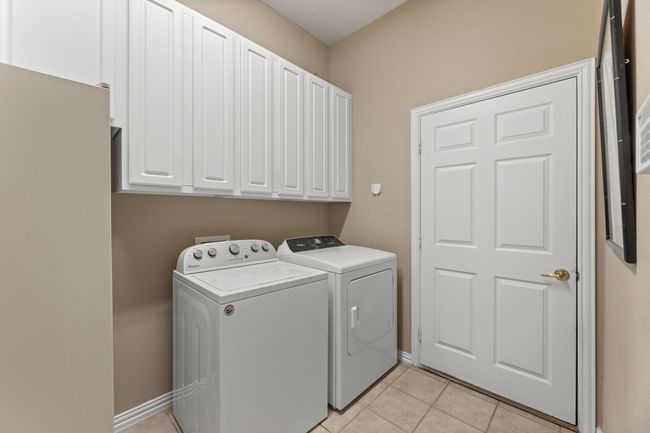 Clothes washing area featuring independent washer and dryer, cabinets, and light tile patterned floors | Image 36